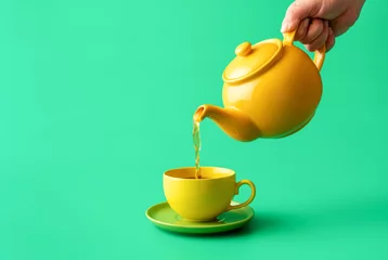 Foto op Plexiglas Pouring tea from a teapot in a cup, isolated on a green background © YesPhotographers
