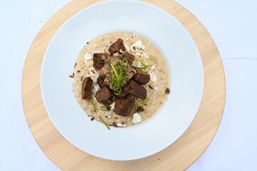 Top view of a creamy dish decorated with hard chucks, cheese and green onions served in white plate