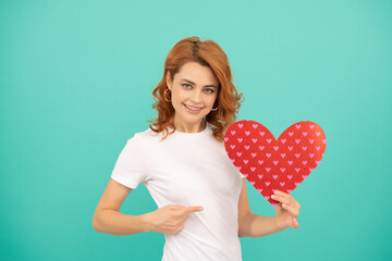 happy young woman with red heart on blue background. pointing finger