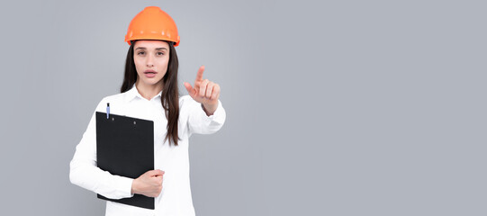 Architect woman in helmet pointing on copy space. Young woman in helmet hold clipboard on gray background. Woman isolated face portrait, banner with mock up copy space.