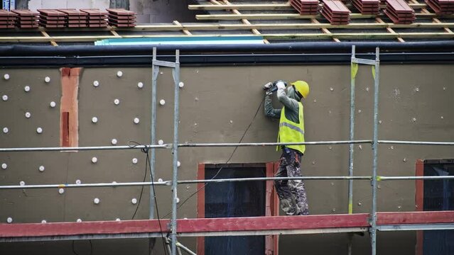Construction Worker Standing on Scaffolding Drilling Hole in Wall Plasterwork