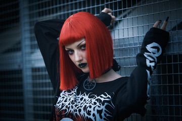 Young urban goth girl with a red hair wig posing outdoors, representing alternative subculture - 545251014