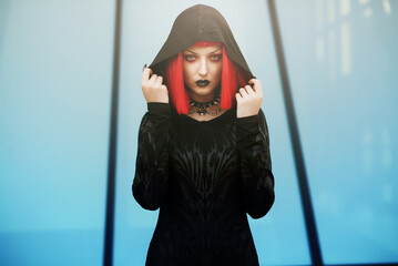 Young urban goth girl with a red hair wig posing outdoors, representing alternative subculture