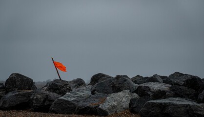 Orange flag wrapped on a stick surrounded by stones on a stormy day