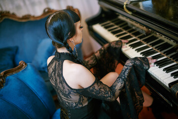 Young gothic girl playing the piano indoors, touching keyboard with her fingers, wearing an old fashion victorian dress