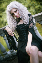 Portrait of a gothic girl, looking like a doll lolita, posing next to an old stone staircase of a...