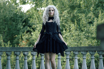 Portrait of a gothic girl, looking like a doll lolita, posing next to an old stone staircase of a...