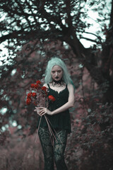 Dark goth girl standing in the forest, holding a bouquet of red roses, posing among the trees and long grass