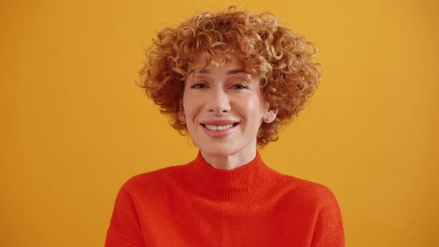 Friendly curly haired adult ginger woman showing shh gesture at the camera in the yellow studio