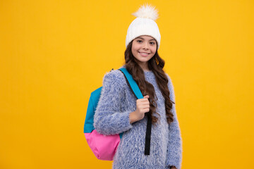 Portrait of school teenage girls in winter hat holding copybooks and backpack over yellow background. Winter school. Happy girl face, positive and smiling emotions.