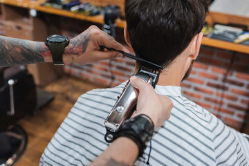 brunette man near tattooed hairdresser trimming his neck with electric hair clipper. - obrazy, fototapety, plakaty