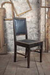 An old oak chair stands in a dirty room, on the old floor next to other vintage things