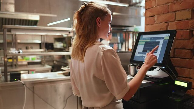 Concentrated blonde woman cashier typing in the order in the restaurant kitchen