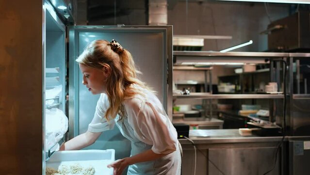 Handsome blonde woman chef gets noodles out of the fridge in the restaurant kitchen