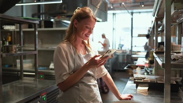 Nice blonde woman chef texting on phone in the restaurant kitchen