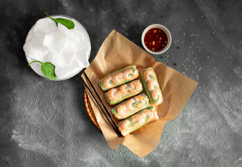 Vietnamese spring rolls with tender chicken, tiger prawns, juicy mango, fresh herbs, rice chips on a black background. Sesame sauce. Healthy natural Vietnamese food.