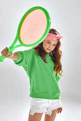 Girl with pink headband shows tennis racquet in studio