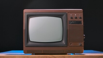 Old TV on a wooden table against black studio background. Brown retro media equipment. Retro TV with a turned off screen. An aged analog apparatus for broadcasting entertainment programs.
