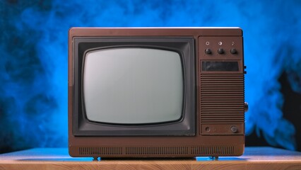 Old TV on a wooden table against black studio background with blue light and smoke. Brown retro...