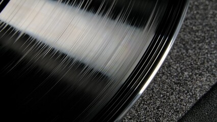 Macro shot of a black glossy grooved vinyl record. An old shiny gramophone record illuminated by light. Vintage vinyl record player. Retro background with vinyl turntable, nostalgia.