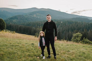 Fototapeta na wymiar Child hugs father in field. Dad and daughter walk in the mountains enjoy autumn and look at nature. The young family spends time together on vacation, outdoors. Father's Day.