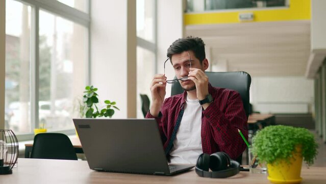 Exhausted customer support service worker removes headphones, finishes work, closes laptop. Tired developer ends working day in office. Video editor freelancer ends project, leaves workplace.
