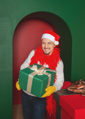 Smiling man wearing Santa hat holding Christmas gift boxes on the red arch background. New Year style