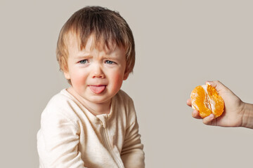 a baby with a food allergy doesn't want to eat an orange, winces, the child is offered an orange