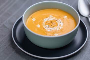 Creamy pumpkin soup garnished with  cooking sauce served in turquoise dish with slice of bread in rustic mood. Seasonal warm food. Autumn Appetiser 