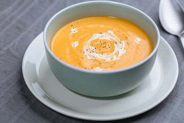 Creamy pumpkin soup garnished with  cooking sauce served in turquoise dish with slice of bread in rustic mood. Seasonal warm food. Autumn Appetiser 