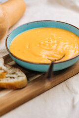 Creamy pumpkin soup garnished with  cooking sauce served in turquoise dish with slice of bread in rustic mood. Seasonal warm food. Autumn Appetiser 