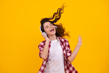 Amazed teenager. Teenager child girl in headphones listening music, wearing stylish casual outfit isolated over yellow background. Excited teen girl.
