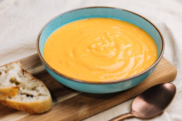 Creamy pumpkin soup garnished with  cooking sauce served in turquoise dish with slice of bread in rustic mood. Seasonal warm food. Autumn Appetiser 
