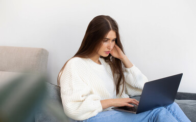 An attractive brunette is sitting at home on the couch and using a laptop. Online training. 