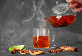 Hot strong tea is poured from a glass teapot into a cup. A cup of freshly brewed black tea with herbs and fruits. Tea ceremony