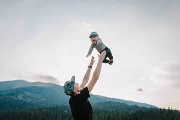 Portrait of father throws up happy son on hands, walking on nature in autumn day. Dad and child...