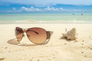 Fototapeta na wymiar Dark sunglasses against a blurred seascape. Sunglasses on a sun-drenched sandy beach with a blurred sea shell nearby.