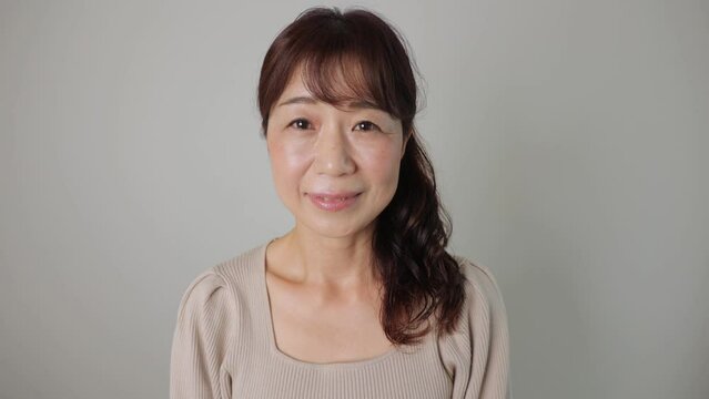 Asian middle aged woman smiles at the camera. Dolly in. White background.