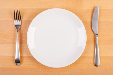 flat lay image of empty white plate, fork and knife on wooden table