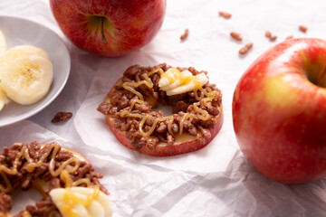 Creative party snack for holidays. Apple rounds with peanut butter, caramel and chocolate flavor puffed rice topping with banana slices. Funny appetizer for kids and adults.