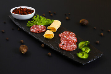 Sliced smoked salami sausage with vegetables and other ingredients on a black stand. Shallow depth of field