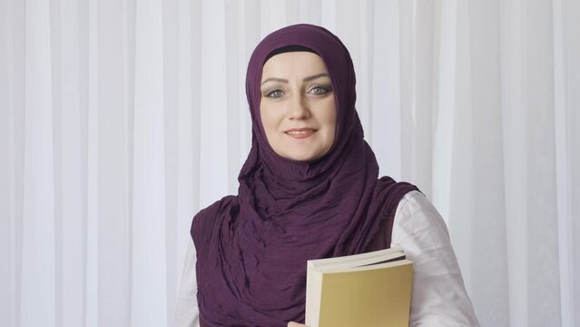 Student woman in hijab poses for camera holding books.
Muslim student woman looking at camera and smiling.
