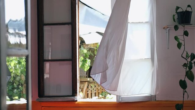White long curtains flying from the wind hanging on an open window on summer day
