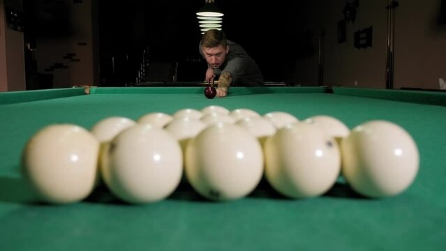 Man playing in billiard in dark billiard room. Man trying to hit the ball in billiard. Billiard room on the background. Young successful handsome man playing in russian pool at bar with friends.