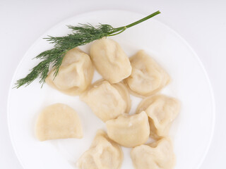 Cooked dumplings on a white plate with dill. Flatlay