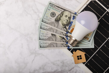 Flat lay composition with solar panel, led lamp, house model and money on  table. Money saving and...