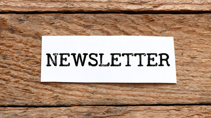 NEWSLETTER word written on a white piece of paper placed on a wooden table.