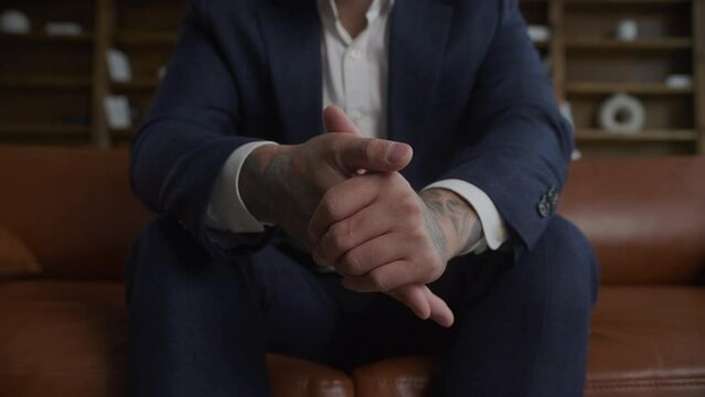 An extreme close-up of a businessman's tattooed hands in a suit squashed in slow motion