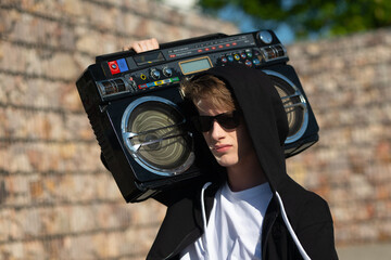 A young man in a white t-shirt and black tracksuit. A boy model with blond hair and white skin with a boombox on his shoulder. A boy in a hood.