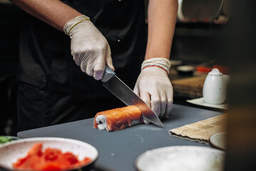 Chef coock cut fresh sushi rolls with sharp knife on the cutting board in restaurant. hands close up